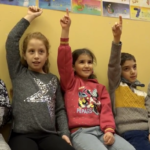 Tre barn rekker opp hånda.