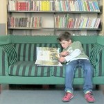En gutt sitter og leser i en grønn sofa.