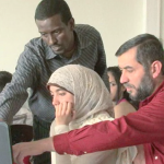 En ung kvinne ser på en dataskjerm sammen med to voksne menn.