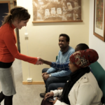 En lærer hilser på en elev. Eleven sitter i en sofa med en voksen på hver side av seg.