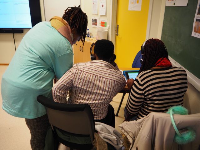 En flerspråklig assistent hjelper to deltakere.