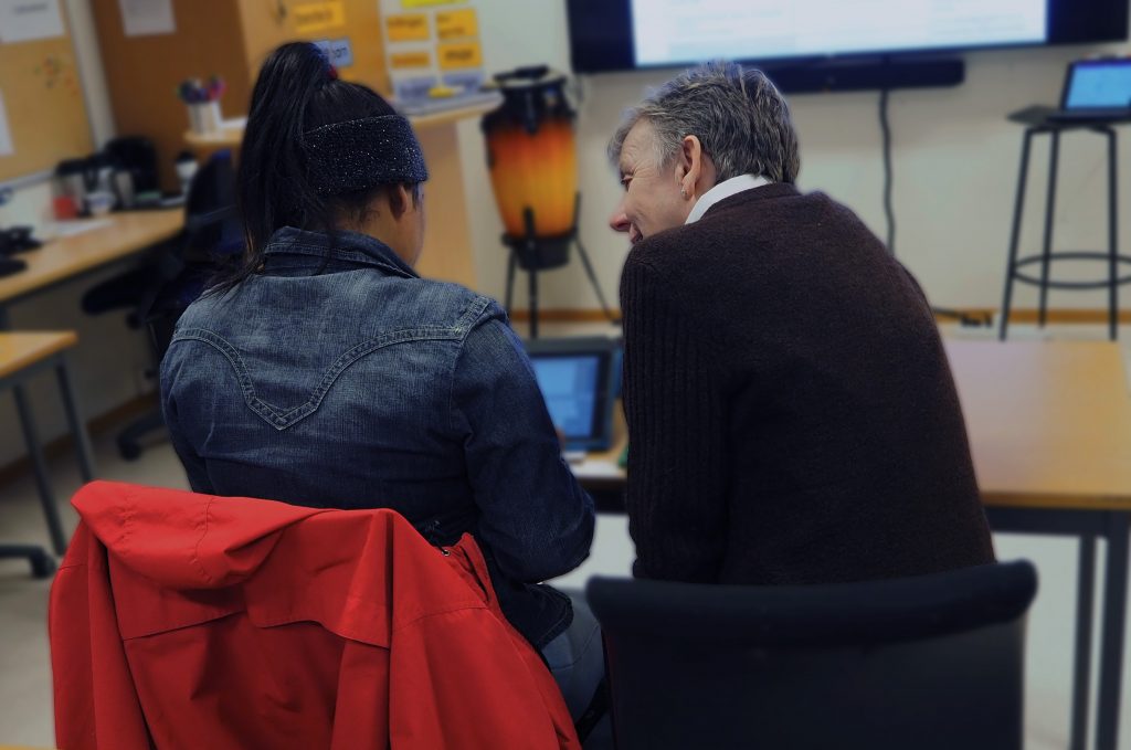 Foto av en deltaker og en lærer som sitter sammen ved en IPdad og diskuterer.