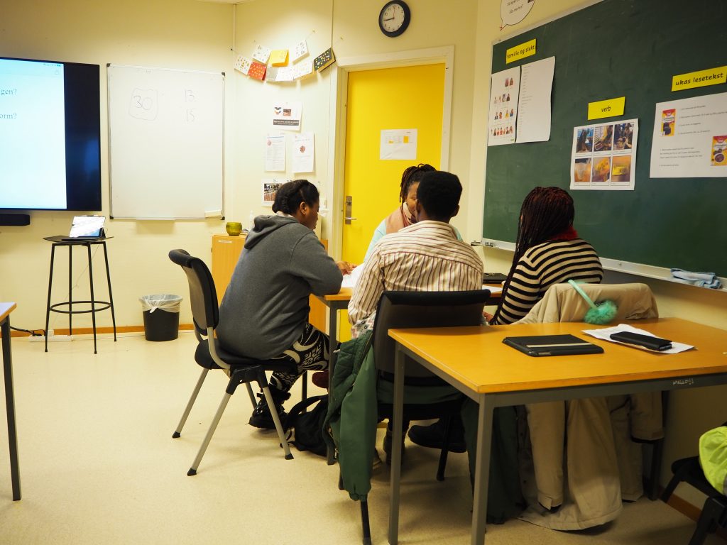 Vi ser fire deltakere med afrikansk opphav som sitter rundt et bord i et klasserom. Deltakerne har felles morsmål.