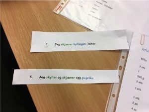 Foto av to papirlapper med setninger. På en står det: Jeg skjærer kyllingen i biter. På den andre står det: Jeg skyller og skjærer opp paprika.