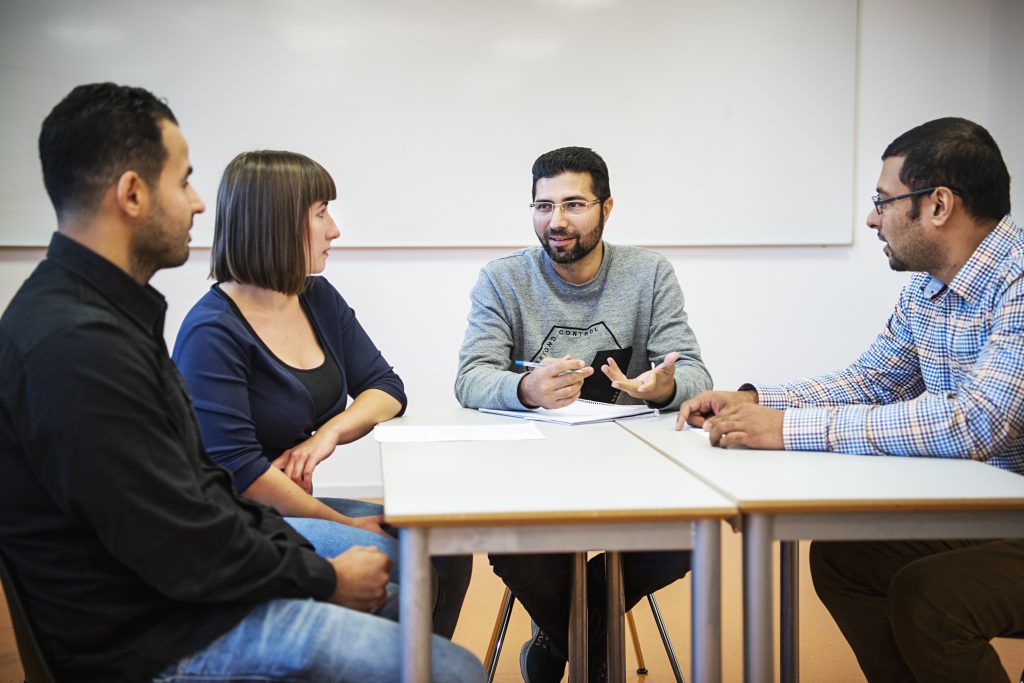 Foto av fire personer som samtaler rundt et bord. En av de fire tolker det som blir sagt.