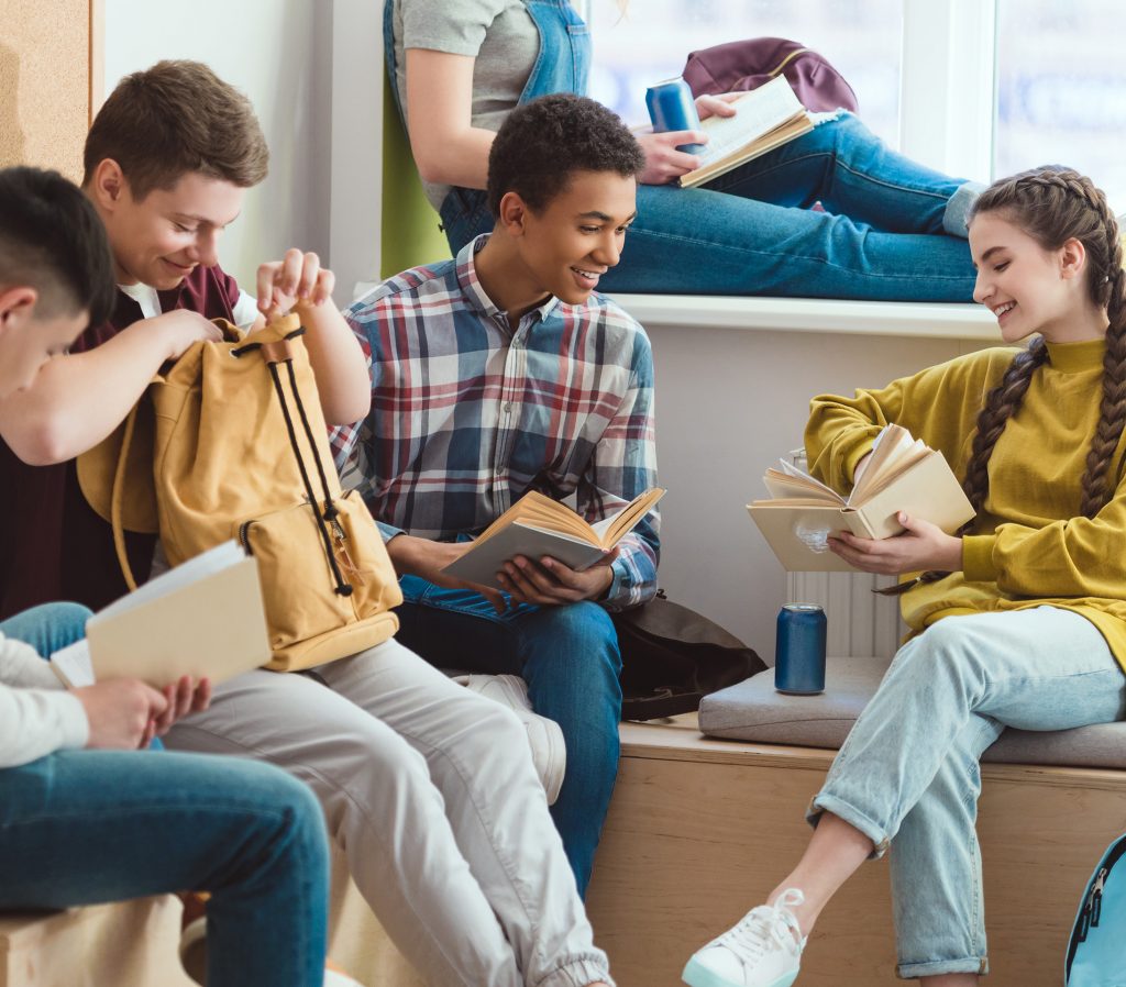 Foto av ungdommer som sitter på en benk med bøker og skolesaker rundt seg.