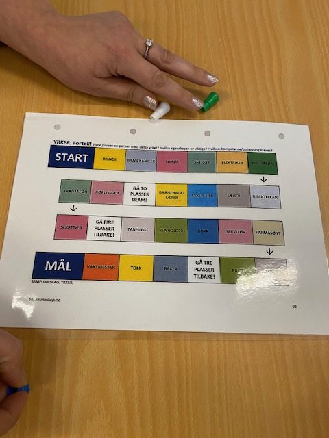 Foto av et brettspill. Vi kan lese start og mål, på noen av rutene står det yrker: bonde, vaktmester, tolk, baker og servitør.