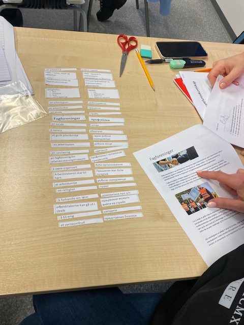 Foto av et bord med to kolonner med ord. En kolonne er på norsk og en på ukrainsk. En deltaker holder et ark med tekst.