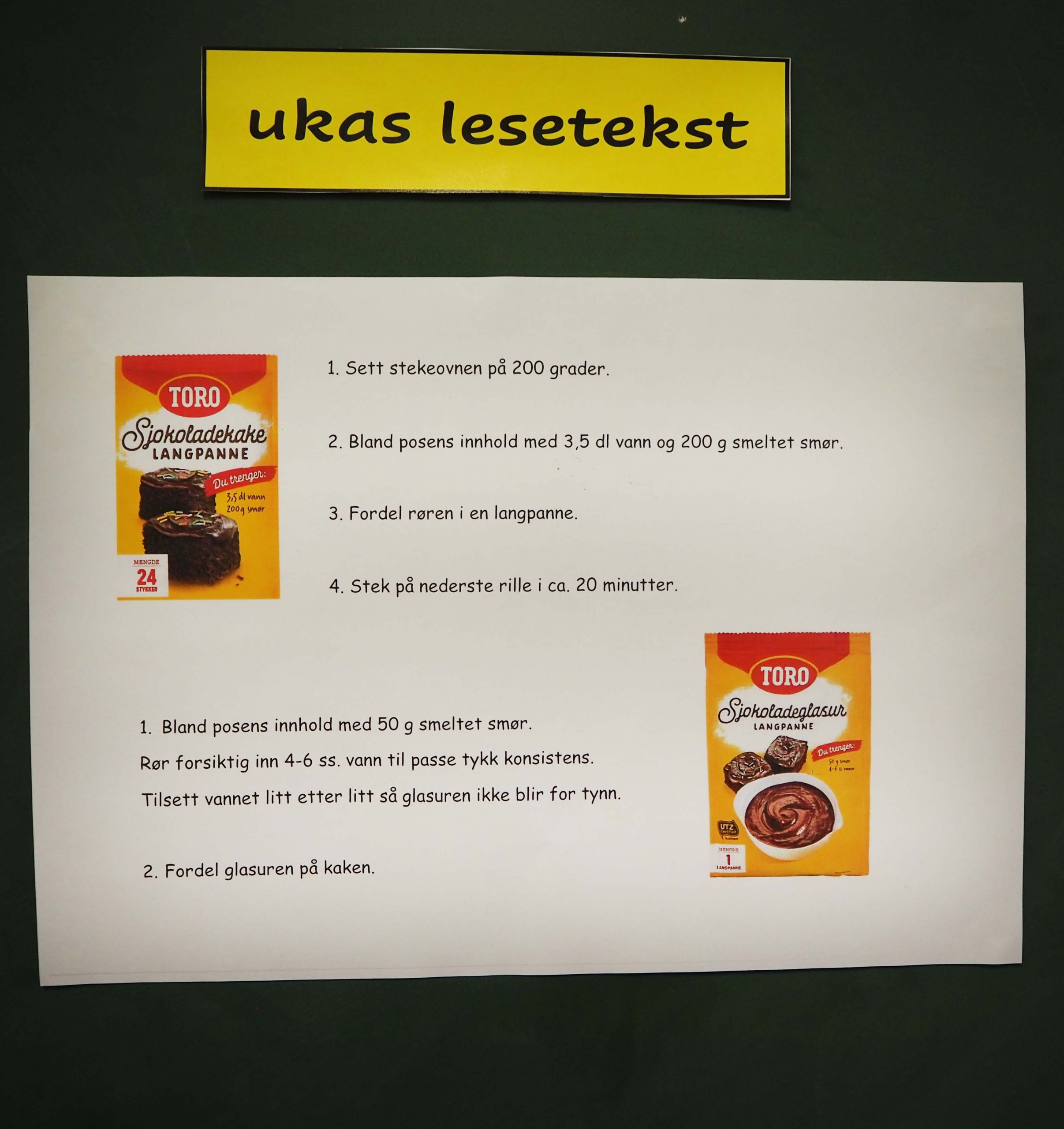 Foto av en tavle. Øverst står det ukas lesetekst på en gul lapp. Under henger en tekst. Det står: 1. Sett stekeovnen på 200 grader. 2. Bland posens innhold med 3,5dl vann og 200 g smeltet smør. 3. Fordel røren i en langpanne. 4. Stek på nederste rille i ca. 20 minutter.