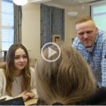 Foto av en lærer og to elever i et klasserom som snakker sammen