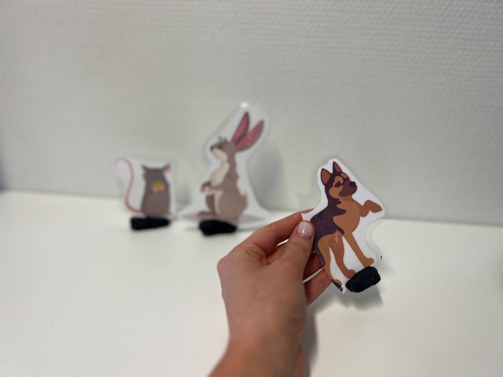 En hånd holder en liten figur sin er klippet ut. To andre figurer står bak.