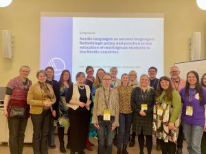 Foto av en gruppe mennesker som står foran en skjerm hvor det står: "Nordic languages as second languages: Rethinking policy and practice in the education of multilingual students in the Nordic countries".