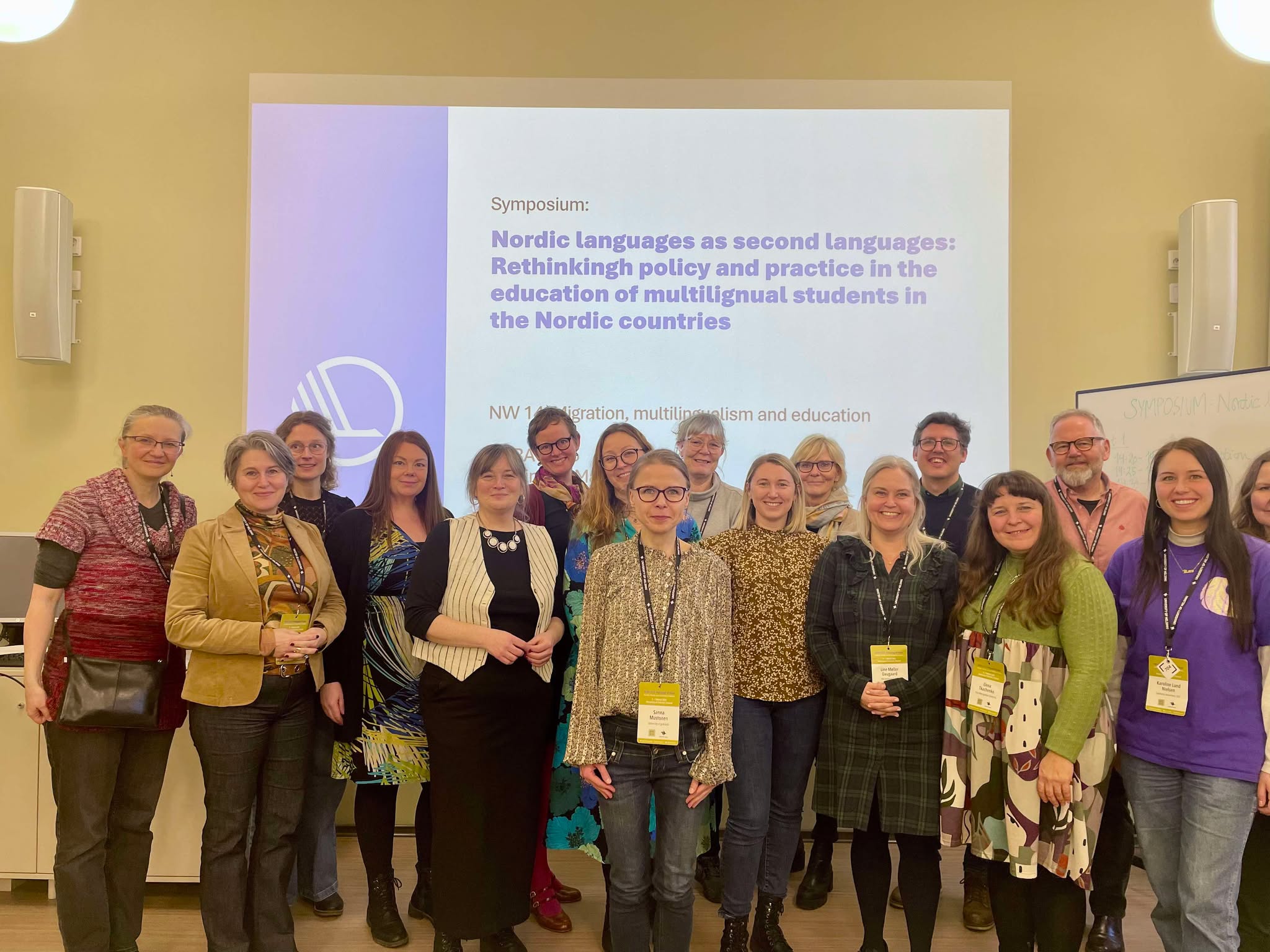 Foto av en gruppe mennesker som står foran en skjerm hvor det står: "Nordic languages as second languages: Rethinking policy and practice in the education of multilingual students in the Nordic countries".