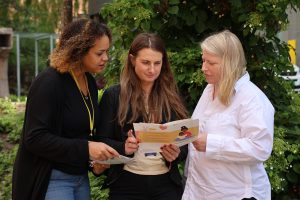 Fotografi av tre kvinner som står og holder en brosjyre mellom seg.