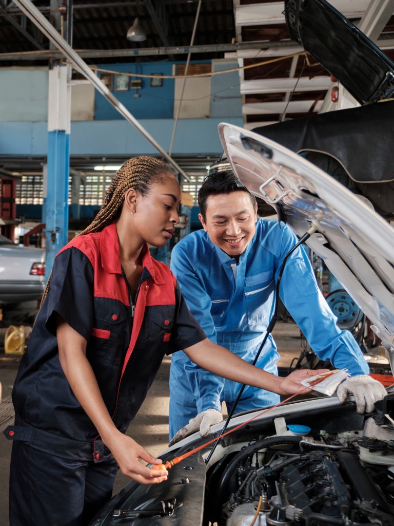 Foto av en elev og en lærer på et bilverksted. Panseret er åpent. Eleven har en peilestang for olje i hendene. Læreren står ved siden av. Bildet illustrerer en læringsfremmende vurderingsituasjon. 