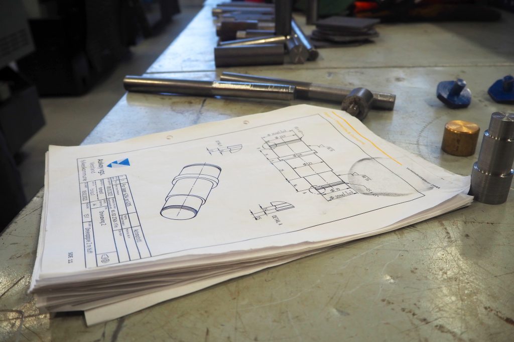 Foto av et undervisningshefte som ligger på en arbeidsbenk i et verksted. Ved siden av heftet ligger noe verktøy og materiale.