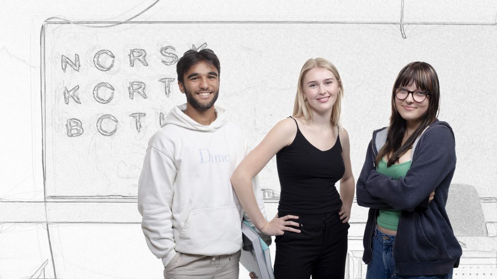 Foto av tre elever står foran en tavle hvor teksten norsk kort botid er skrevet.