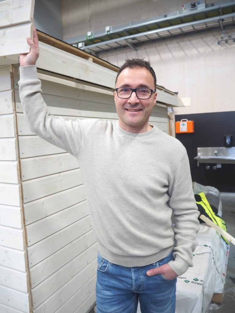 Portrettfoto av Helge som står ved en vegg elevene har bygd på verkstedet.