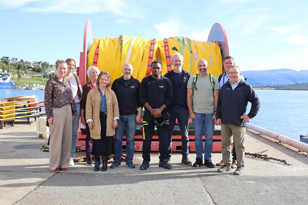 Foto av personer som står foran en stor kabeltønne ved bedriften NOFI.