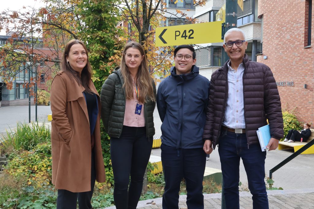 Fire personer står oppstilt ute og smiler til kamera.