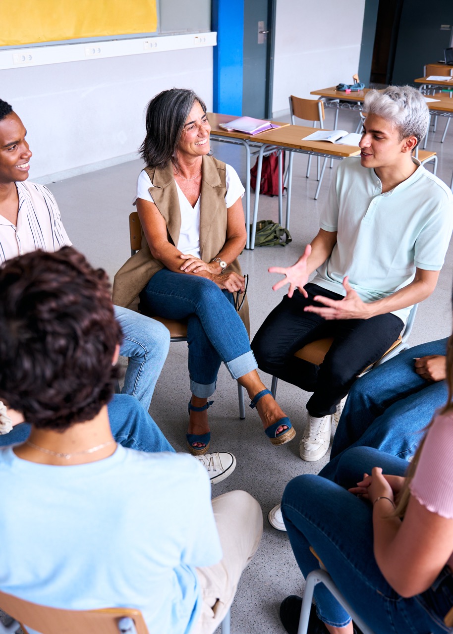 Foto av en lærer og elever som sitter i en sirkel i klasserommet og samtaler sammen. Bildet illustrerer dialogisk undervisning i klasserommet.